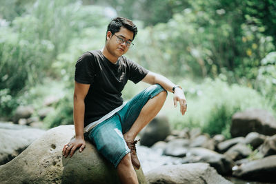 Young man looking away while sitting on rock