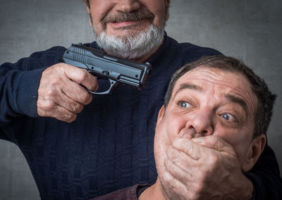 Senior man aiming gun while covering victims mouth
