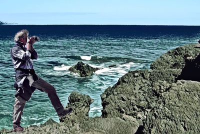 People photographing at sea shore against sky