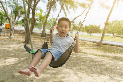 Portrait of boy screaming while sitting on swing at playground