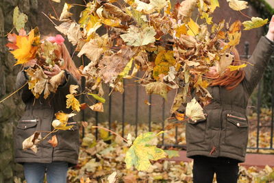  girls throwing dry leaves while standing outdoors 