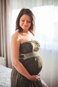 Pregnant woman in dress against window in bright room