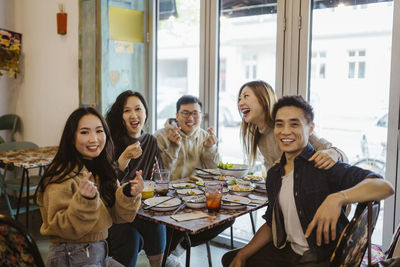 Happy multiracial male and female friends gesturing and laughing during lunch at restaurant