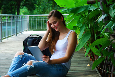 Young woman using digital tablet while sitting on boardwalk