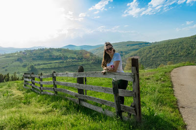 Woman standing on field by fence against sky