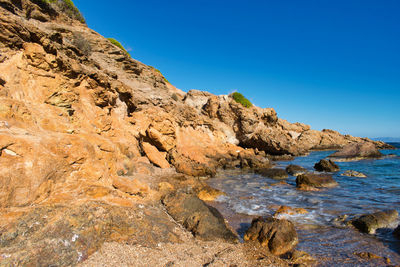 Rock formation in sea against clear blue sky