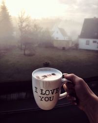 Close-up of hand holding coffee cup against sky