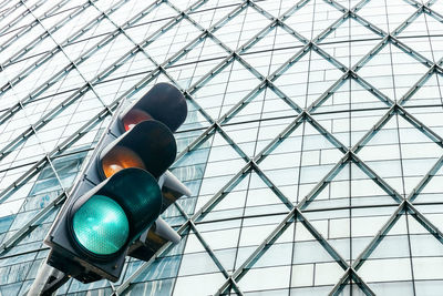 Low angle view of traffic lights against glass building in the city