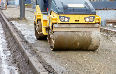 Front view of a yellow compact road roller tamping the foot of the sidewalk at a construction site.