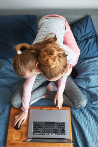 Girl embracing sister studying at laptop