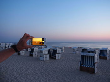 Man photographing on beach against sky during sunset