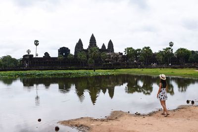 Rear view of woman standing by lake at angkor wat against sky