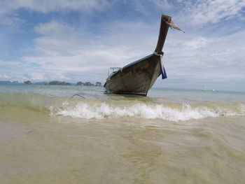 Boat anchored at beach against cloudy sky