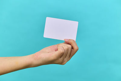 Cropped hand of woman holding paper against blue background