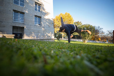 Low angle view of man jumping on field by building