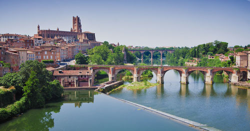 Bridge over river by buildings against clear sky