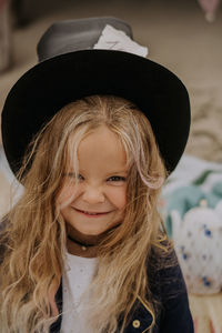 Child girl in jacket and top hat smiling and looking at the camera at the beach