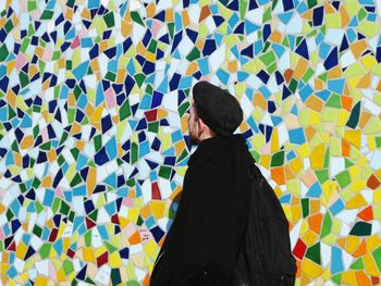 Young man standing against colorful mosaic wall