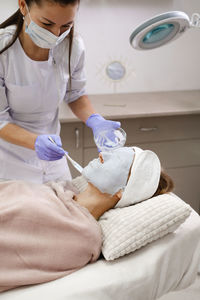 Cosmetologist apply skin mask with brush, care and treatment procedure in modern aesthetic clinic