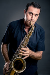 Portrait of mature man playing saxophone against black background