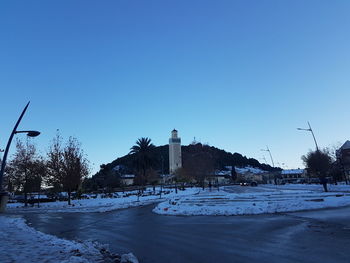 Snow covered field by building against clear blue sky