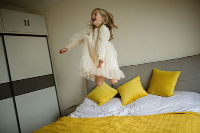 Beautiful little girl in stylish dress jumping on the bed with white blanket at home. stay at home 
