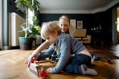 Mother and daughter playing with toy train on hardwood floor in living room at home