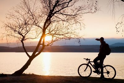 Young man cyclist silhouette on blue sky and sunset background on the beach.