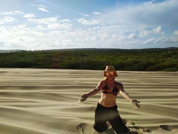 Portrait of woman spilling sand at beach against sky