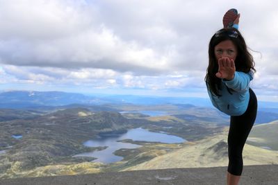 Woman exercising against cloudy sky