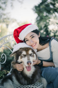 Portrait of smiling woman wearing santa hat with dog sitting outdoors