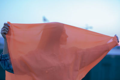 Woman holding orange textile against sky