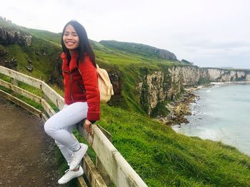 Portrait of smiling woman sitting on railing against sea