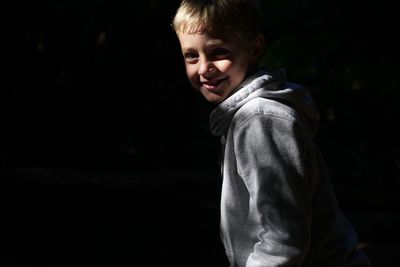 Portrait of smiling boy standing against black background