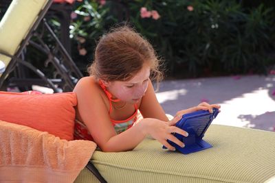 Girl using digital tablet while lying on seat