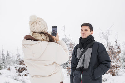 A young girl photographs a guy on the phone in a winter forest.