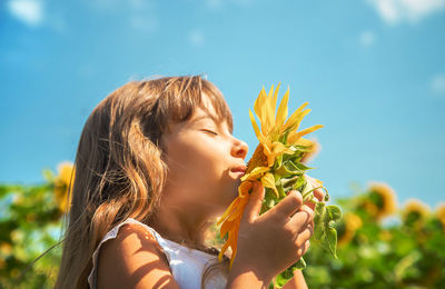 Portrait of young woman holding flower against sky