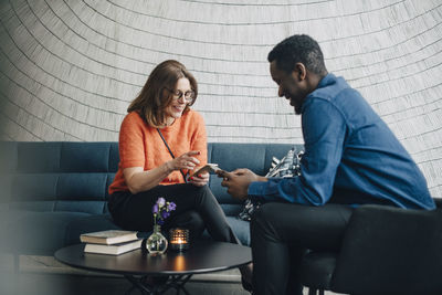 Smiling business colleagues using mobile phones while sitting on couch during conference