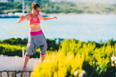 Woman with plastic hoop dancing against lake