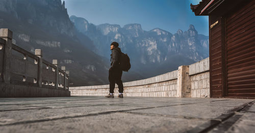 Woman standing on wall by mountain against sky