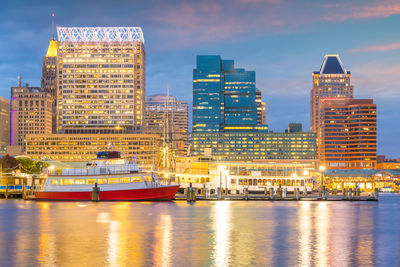 Illuminated buildings by river against sky in city