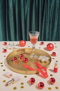 New year party composition with cocktail glass, red baubles, makeup, confetti and decoration.