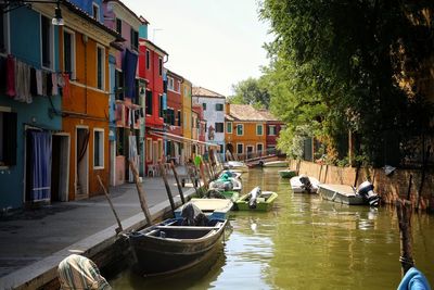 Boats moored in canal by city against sky