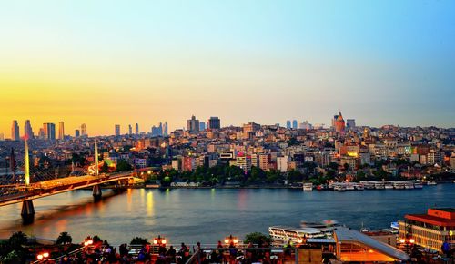 Panoramic view of illuminated buildings by river against sky during sunset