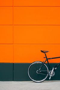 Cropped image of bicycle parked on footpath by orange wall