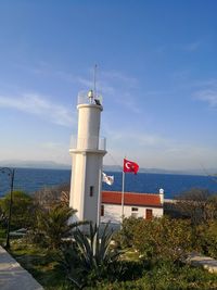 Lighthouse by turkish flag against sea and blue sky