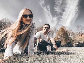 Young woman wearing sunglasses sitting on plants against sky