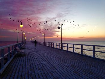 Rear view of silhouette man standing on pier over sea at sunset