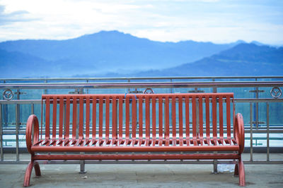 Empty bench by railing against sky