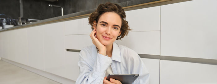 Portrait of young woman using mobile phone while standing at home